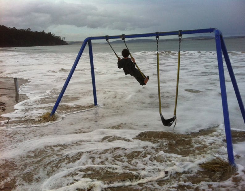 Child swinging on play equipment - while the ocean laps beneath the swing from inundation